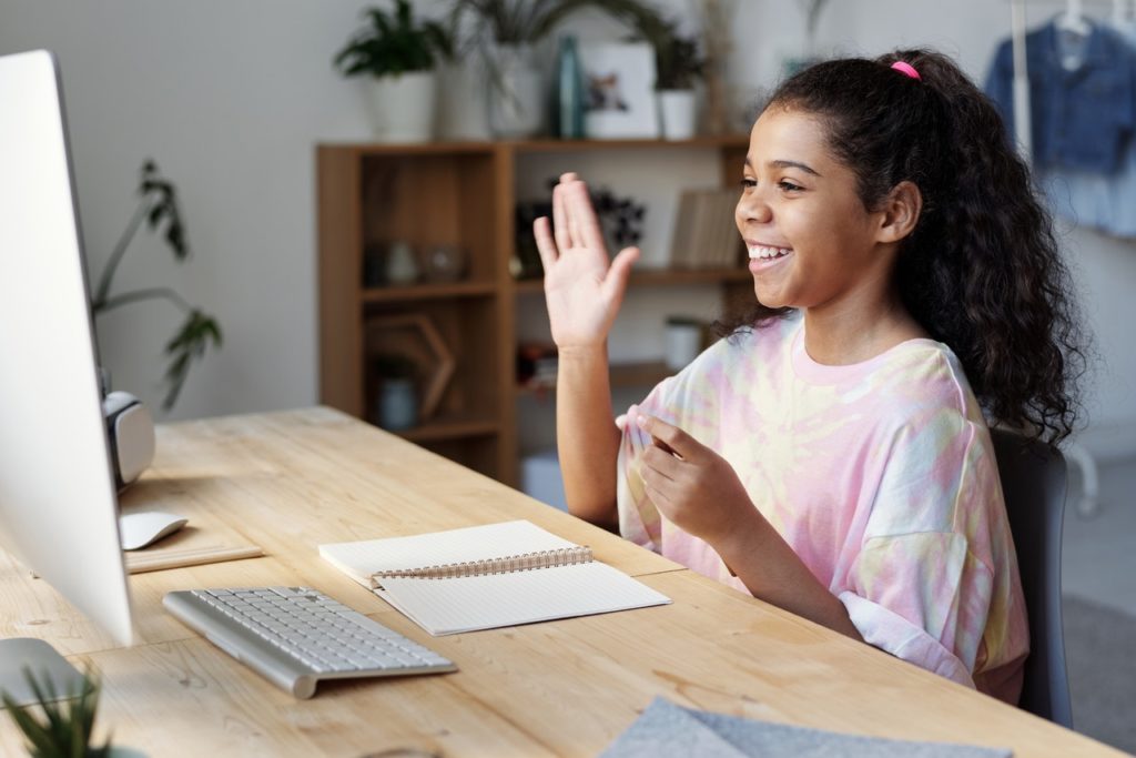 young girl raising her hand reciting during online class
