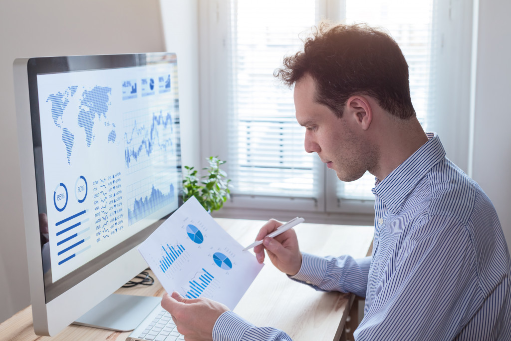 Man wearing shirt sitting in front of computer looking at the business charts to analyze them